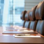 Close-up of a conference table with notepads and pens neatly arranged in front of brown leather chairs in a meeting room.